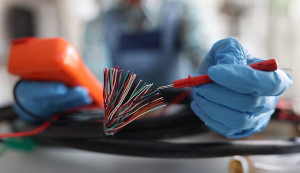 Master repairman testing multicolored wires from cable using tester closeup. Electronics repair concept