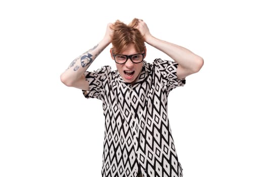 a young european male student with red hair is wearing a shirt with a diamond pattern has a tattoo on his arms.