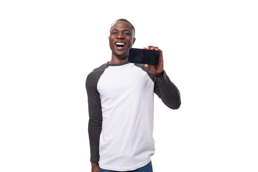 young american guy with short haircut dressed in a long-sleeve sweater reports the news pointing with his hand at a smartphone with a mock-up for advertising.