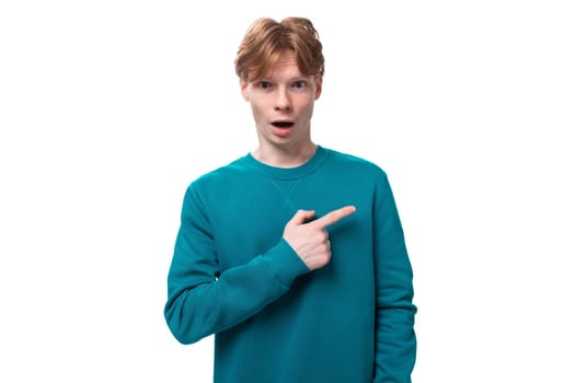 a young guy with short red hair dressed in a blue pullover points his hand to the side.