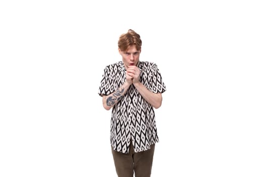 a young caucasian man with red hair with a tattoo dressed in a summer black and white shirt is waiting and thinking against the background with copy space.