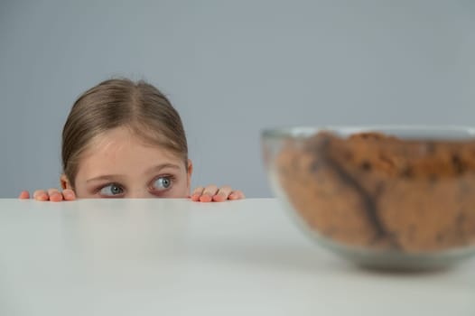 A little girl tries to steal cookies from the table