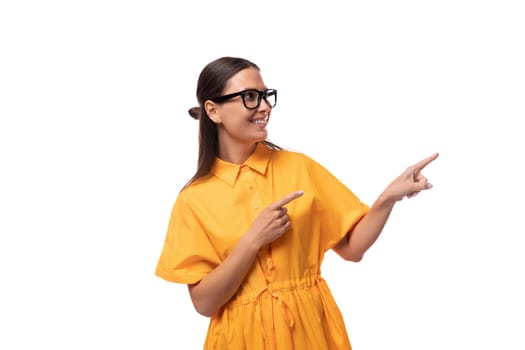 young pretty brunette lady dressed in a yellow dress shows her hand to the side.