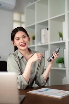 Asian businesswoman using a calculator and working on her tasks on her laptop at home.