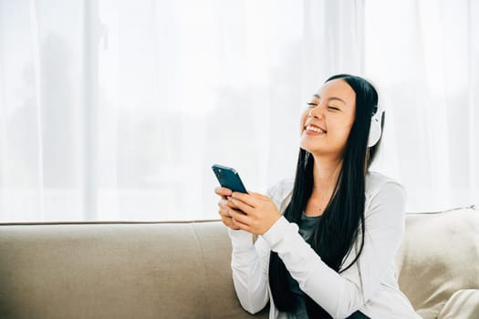 Young woman on sofa enjoys leisure time listens to music on smartphone with headphones. Embracing relaxation enjoyment and modern technology at home.