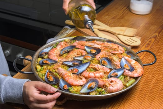 Pouring olive oil into a seafood paella, enhancing the flavors of this classic Spanish dish, typical Spanish cuisine, Majorca, Balearic Islands, Spain,