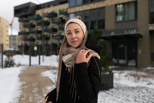 Well-groomed young woman dressed in a winter black coat with a scarf in an urban environment.