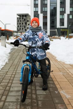 Caucasian boy dressed in a winter jacket rides a bicycle.