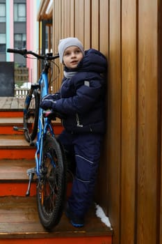 European boy dressed in winter clothes took his bike outside.
