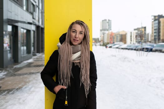 A well-groomed young woman with blond dreadlocks walks down the street in the cold.