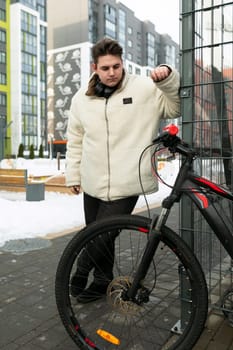 A young European man with a winter jacket walks around the city with a bicycle.