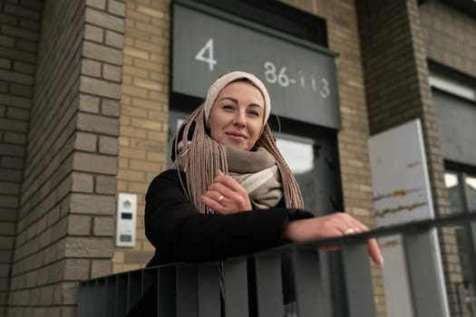 Smiling cute woman with blond dreadlocks wearing a black long winter jacket.