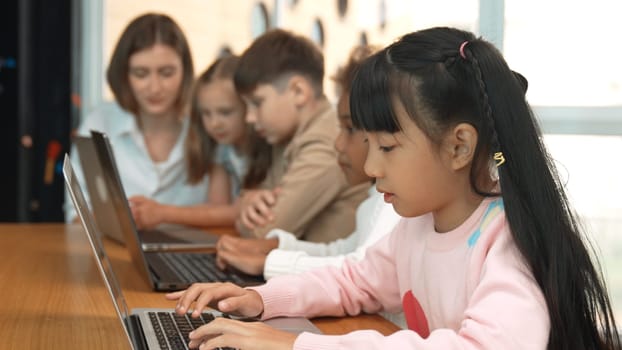 Smart asian girl working on laptop and turn head to doing ok or okay at camera. Diverse children coding or programing engineering code or prompt by using computer in STEM technology class. Erudition.