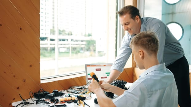 Caucasian teacher help student fixing car model and giving advise for programing system or coding prompt while highschool boy listen and use equipment to repair robot at STEM classroom. Edification.