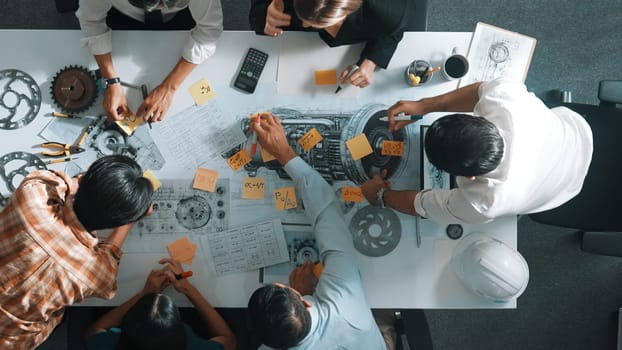 Top view of smart engineer team in casual cloth talking about turbine engine structure at table with metal gear, calculator, sticky notes. Group of technician taking a note in meeting. Alimentation.