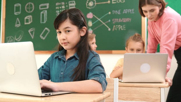 Smart asian girl looking at camera while coding engineering prompt. Multicultural student learning about generated AI while teacher teaching about system or checking classwork at STEM class. Pedagogy.