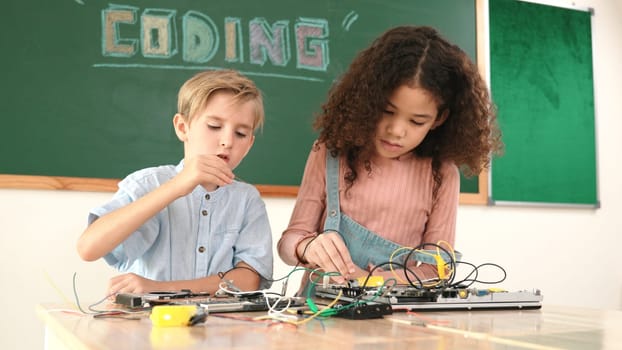 Smart girl standing while fixing electronic board by using screwdriver. Happy student and happy caucasian boy working together to inspect electric system. Curious children working on board. Pedagogy.