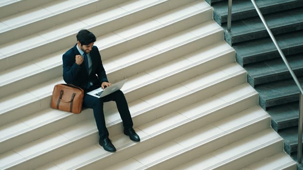 Top view business man celebrate successful project while sitting at stairs. Smart project manager getting new gob, getting promotion, increasing sales while calling friends by using laptop. Exultant.