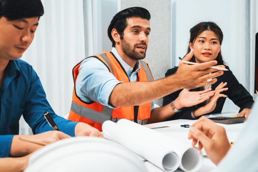 Diverse group of civil engineer and client working together on architectural project, reviewing construction plan and building blueprint at meeting table. Prudent