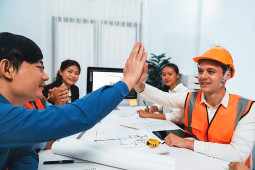 Diverse group of civil engineer and client celebrate and high five after make successful agreement on architectural project, reviewing construction plan and building blueprint at meeting table.Prudent