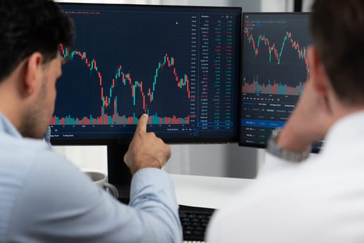 Investor stock trading with serious face sharing with coworker while drinking coffee by using smartphone and pc to show dynamic database of trend graph. Monitor showing investment exchange. Sellable.