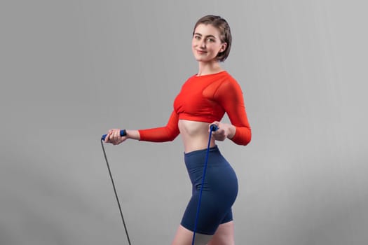 Full body length gaiety shot athletic and sporty young woman with fitness skipping rope in standing posture on isolated background. Healthy active and body care lifestyle.