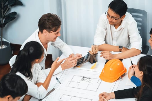 Diverse group of civil engineer and client working together on architectural project, building blueprint and calculate risk reduction for construction project at meeting table. Prudent