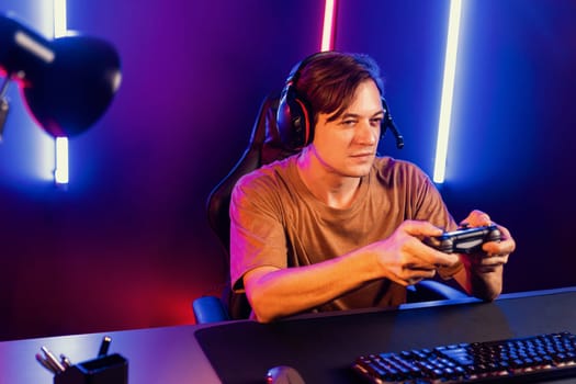 Enjoy smart gaming streamer with control joystick, playing game online of live streaming social media group with team skilled players on computer at modern technology cyber neon light room. Pecuniary.