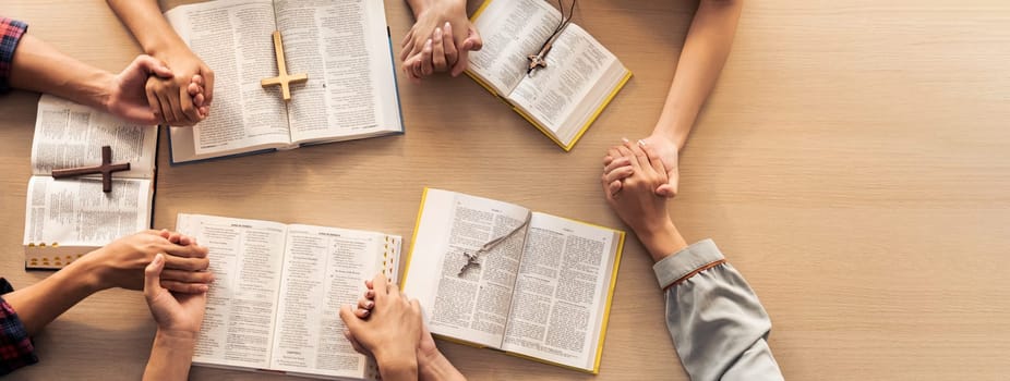 Cropped image of group of people praying together while holding hand on holy bible book at wooden church. Concept of hope, religion, faith, christianity and god blessing. Top view. Burgeoning.