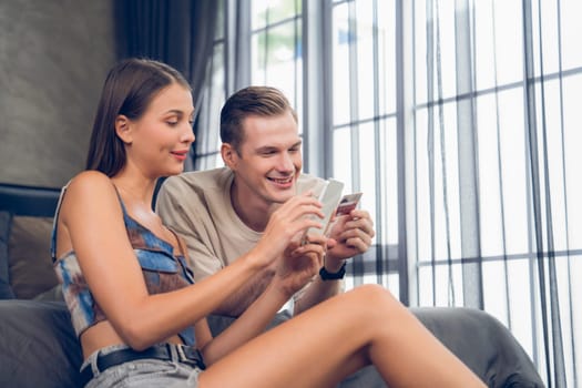 Young couple sit in the home bedroom using online payment app and digital wallet on smartphone to pay with credit card. E commerce shopping and modern purchasing via mobile internet. Unveiling