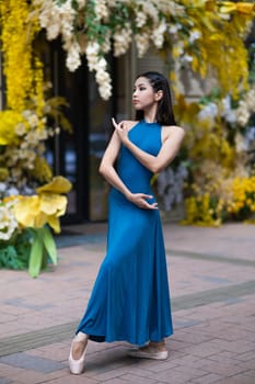 Beautiful Asian ballerina posing against the backdrop of a building decorated with flowers. Vertical photo