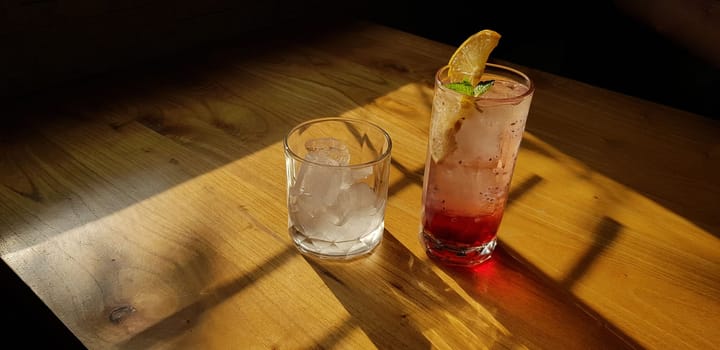 Transparent Glasses with sweet drinks inside with colorful drink, with shadow and table background with ice cubes on a bar restaurant