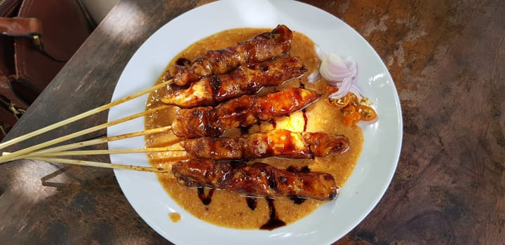 Chicken satay or Indonesian sate ayam, grilled chicken satay with peanut and soy sauce completed with chili and onion, indonesian delicacy