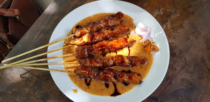 Chicken satay or Indonesian sate ayam, grilled chicken satay with peanut and soy sauce completed with chili and onion, indonesian delicacy