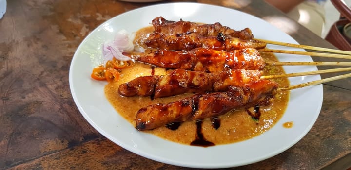 Chicken satay or Indonesian sate ayam, grilled chicken satay with peanut and soy sauce completed with chili and onion, indonesian delicacy