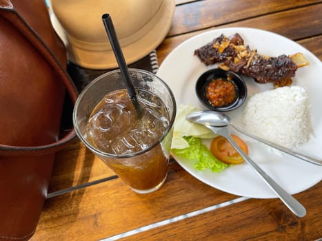 Spicy hot grilled honey roasted spare ribs from summer BBQ served with hot chili paste and rice also ice tea served in white plate