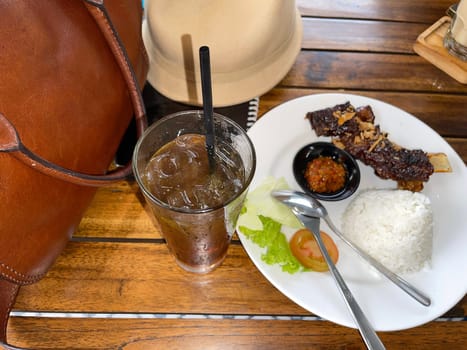 Spicy hot grilled honey roasted spare ribs from summer BBQ served with hot chili paste and rice also ice tea served in white plate