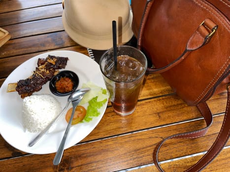 Spicy hot grilled honey roasted spare ribs from summer BBQ served with hot chili paste and rice also ice tea served in white plate