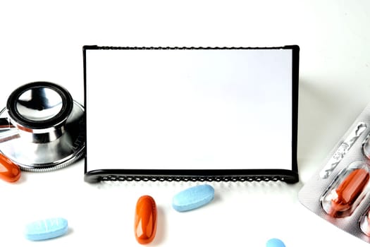 A white card on a black stand on a white background. There are pills next to the stethoscope. A place to copy