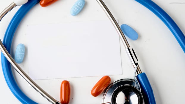 A white card on a white background. A stethoscope and pills . Copy space