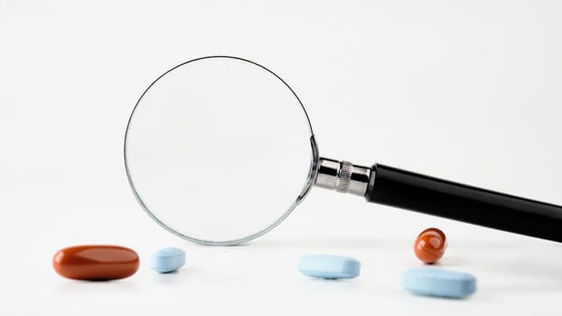 Magnifier on a white background with pills in the foreground. A conceptual photo. A place to copy.