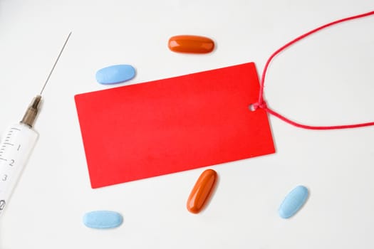 A red card on a white background. There are pills and a syringe nearby. A place to copy. Concept photo