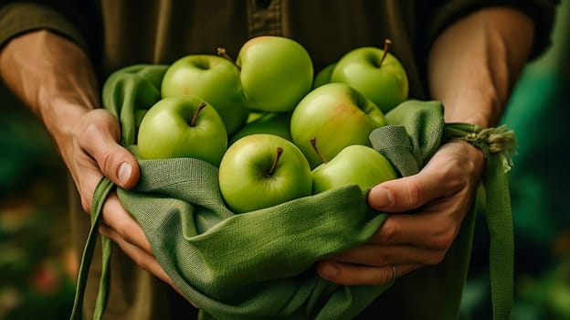 A man holds in his hands a large number of green apples in a bag made of natural fabric. The concept of recycling, saving, fighting plastic, proper nutrition, healthy lifestyle, diet, veganism, vegetarianism, gardening and farming, fresh fruit