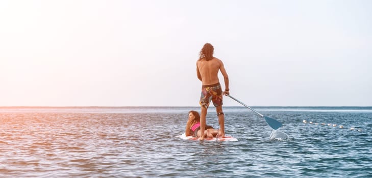 Sea woman and man on sup. Silhouette of happy young woman and man, surfing on SUP board, confident paddling through water surface. Idyllic sunset. Active lifestyle at sea or river