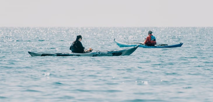 Happy smiling woman in kayak on ocean, paddling with wooden oar. Calm sea water and horizon in background