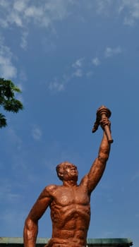 Surakarta, Indonesia, 20th June 2023, Statue of spirit of sport in a form of man holding torch against blue sky, Patung obor manahan located at the Manahan stadium Surakarta, symbol of the spirit of sports