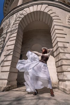 Stylish woman building city. A dancer in a long white skirt dances in front of a building with an arch. The skirt develops in the wind
