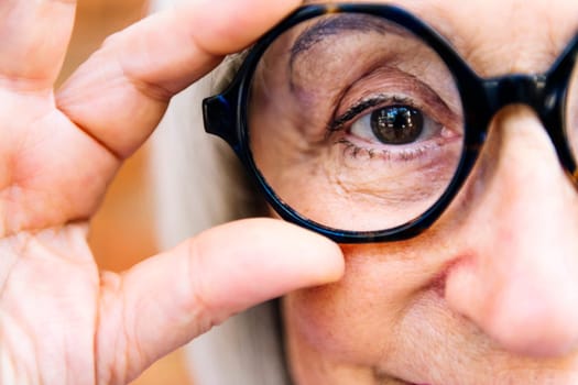 close up of the eye of a senior woman putting on glasses looking at camera, concept of eye health in elderly people and active lifestyle