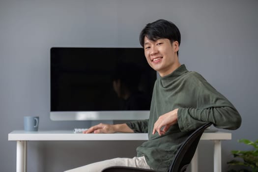 Young Asian student smiling happily at computer with blank screen on table.