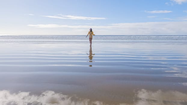 Little girl, braving the cold, joyfully runs in her swimsuit across the beach during winter.